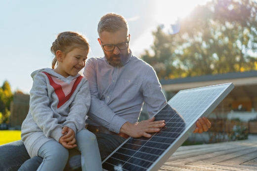Zwei Personen sitzen im Freien auf einer Holzplattform, eine Person hält ein Solarpanel.
